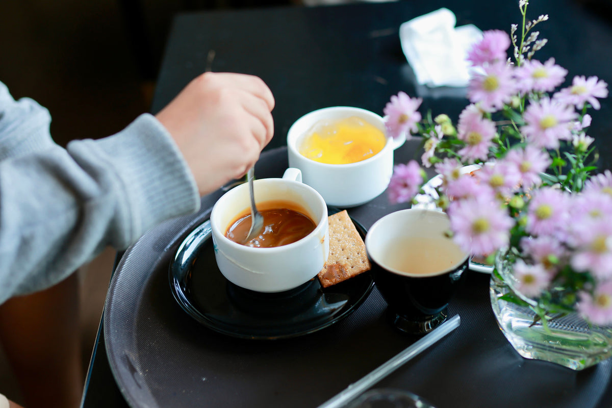 A small space hot drink setup with cups of tea and coffee on a dark tray beside fresh flowers