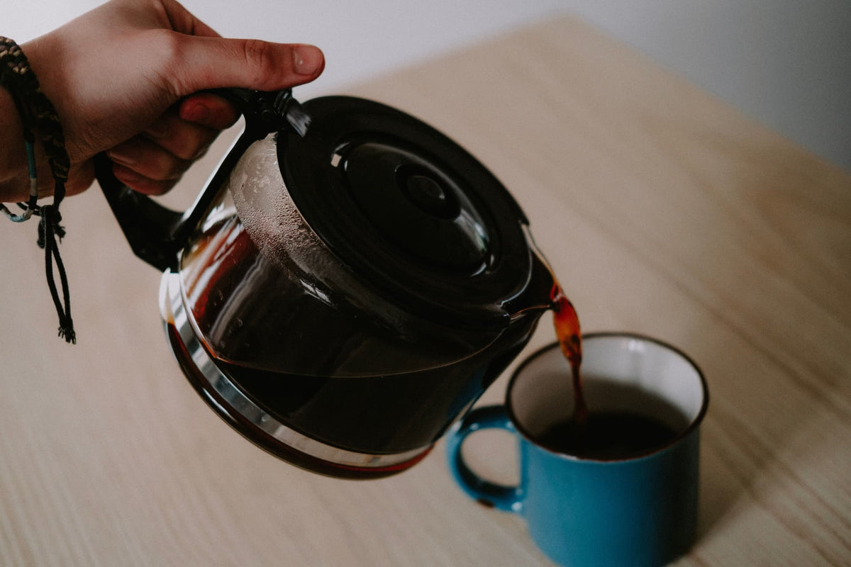 Hot tea being poured from a glass kettle into a blue mug